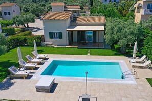 Ein Swimmingpool mit Liegestühlen, eine überdachte Terrasse und ein Haus mit einem Ziegeldach.