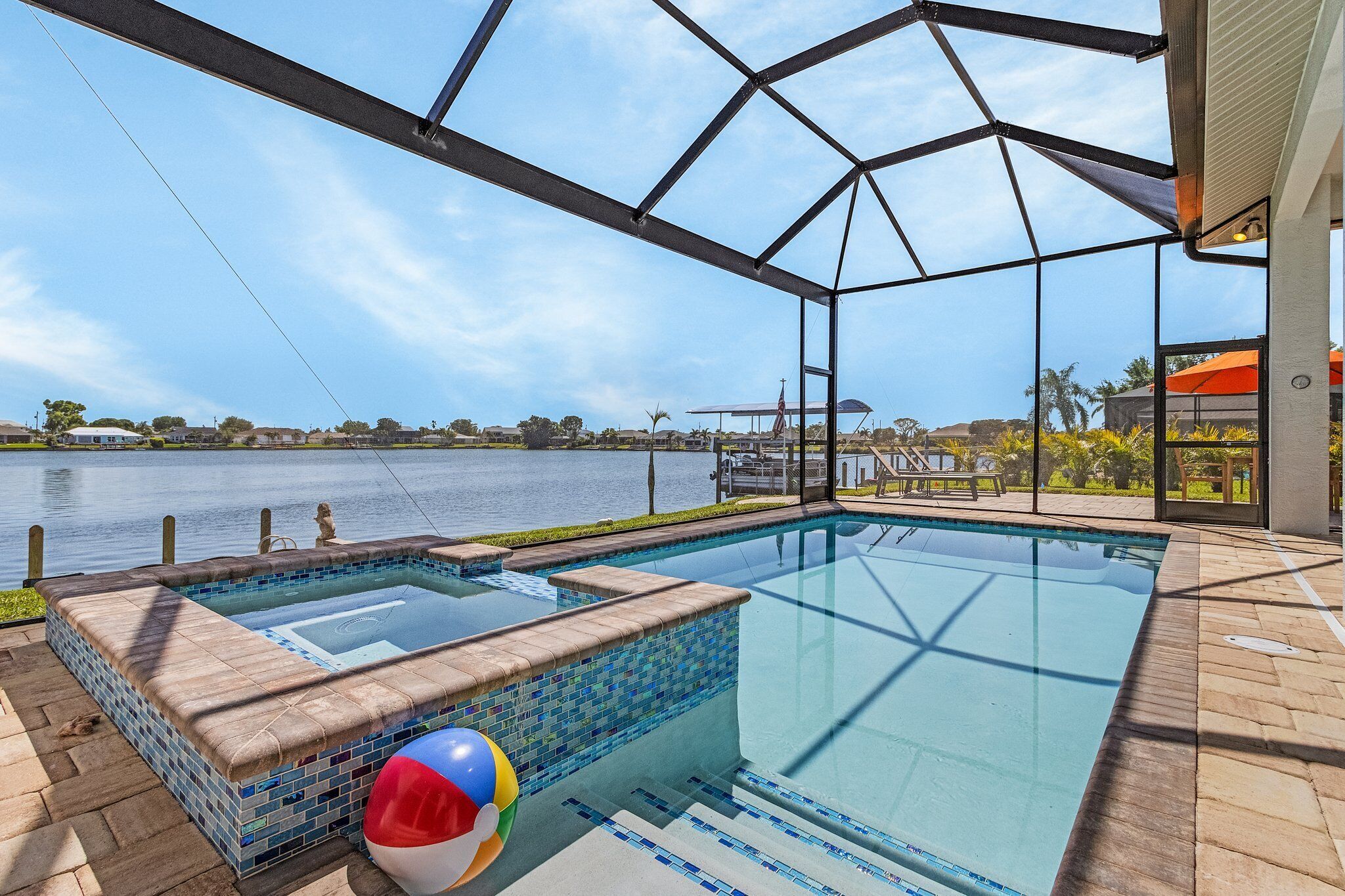 Piscina con vistas a un lago, un jacuzzi y una terraza cubierta.