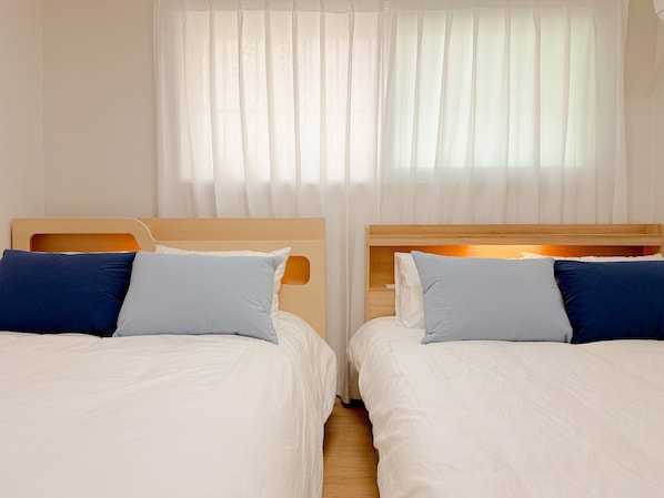 Dos camas individuales con cabeceros de madera, ropa de cama blanca y almohadas azules.