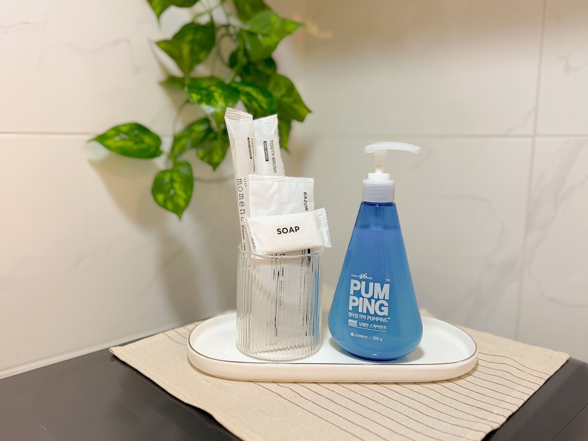 Casa de banho com dispensador de sabonete em vidro transparente, um frasco de sabonete azul e uma toalha branca sobre um tabuleiro branco.