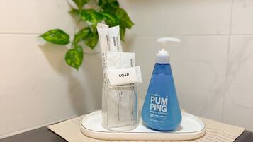 Casa de banho com dispensador de sabonete em vidro transparente, um frasco de sabonete azul e uma toalha branca sobre um tabuleiro branco.