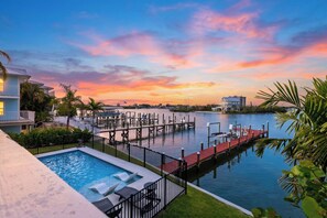 A swimming pool with lounge chairs, a dock extending into the water, and a sunset view. - Private Pool + Dock + Bay Views | Walk to Beach + Times Square | Sunset Slip (Fort Myers Beach)