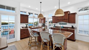Una cocina amplia con ventanas grandes, una isla central, sillas de mimbre y armarios de madera.
