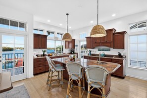 A spacious kitchen with large windows, a central island, wicker chairs, and wooden cabinets. - Private Pool + Dock + Bay Views | Walk to Beach + Times Square | Sunset Slip (Fort Myers Beach)