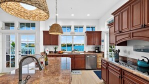 Cocina con una isla grande, electrodomésticos de acero inoxidable, gabinetes de madera y vista al océano.