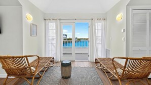 Una habitación con dos sillas de mimbre, una mesa redonda en el centro y vistas a un balcón con piscina a través de un ventanal.