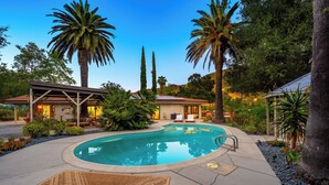 Una piscina con una pérgola, palmeras y un edificio de techo inclinado.