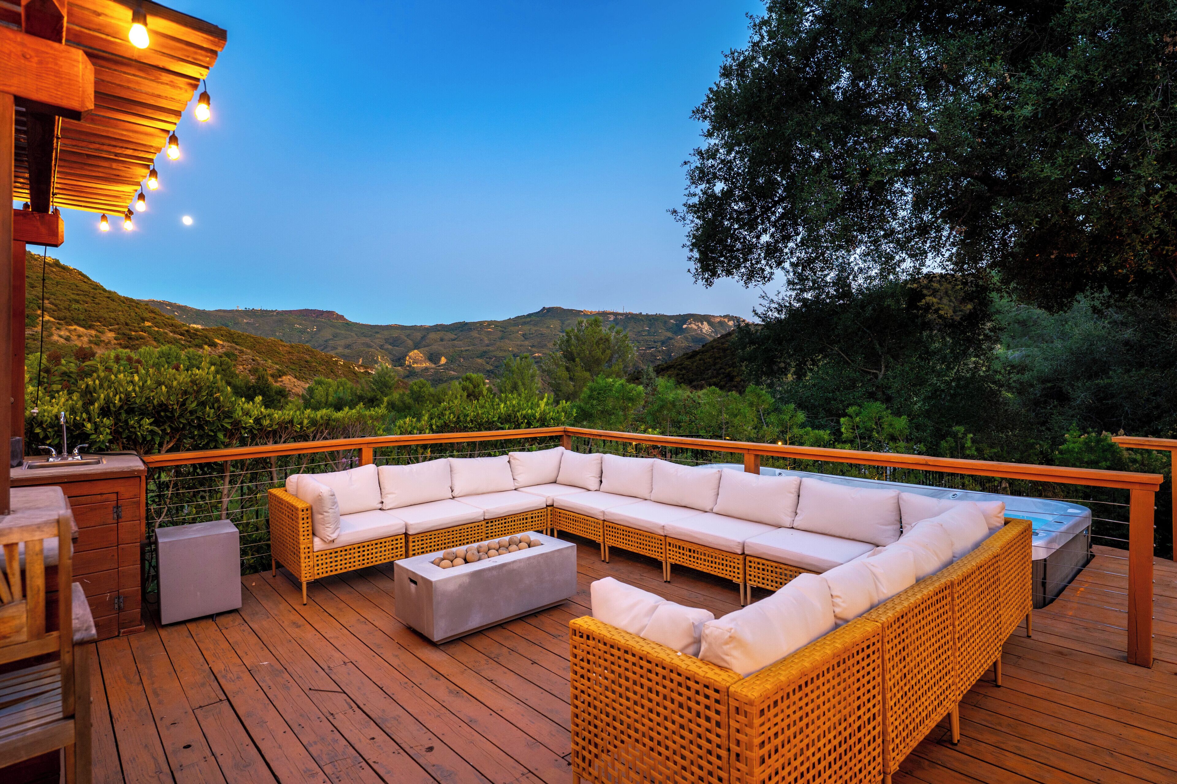 A wooden deck with a sectional sofa, a fire pit, and a hot tub.