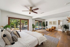 Ein geräumiges Schlafzimmer mit einem großen Bett, einem Deckenventilator und Gartenblick durch Glastüren.