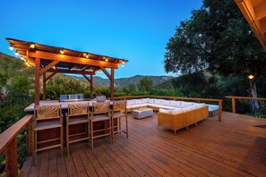 Eine Holzterrasse mit Gartenmöbeln, eine Pergola mit Lichterketten und Blick auf die Hügel.