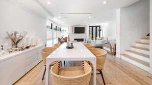 A modern interior with a central dining table, wicker chairs, a fireplace, and a staircase. - Rooftop Deck + Firepit + Wet Bar | Walk to Beach + Trail | Saltaire (Marina Del Rey)