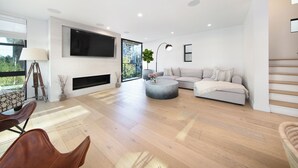 A modern living room with a flat-screen TV, a fireplace, a sofa, a coffee table, and a staircase. - Rooftop Deck + Firepit + Wet Bar | Walk to Beach + Trail | Saltaire (Marina Del Rey)