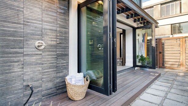 A modern house with a sliding glass door, a wooden deck, and a metal gate. - Rooftop Deck + Firepit + Wet Bar | Walk to Beach + Trail | Saltaire (Marina Del Rey)
