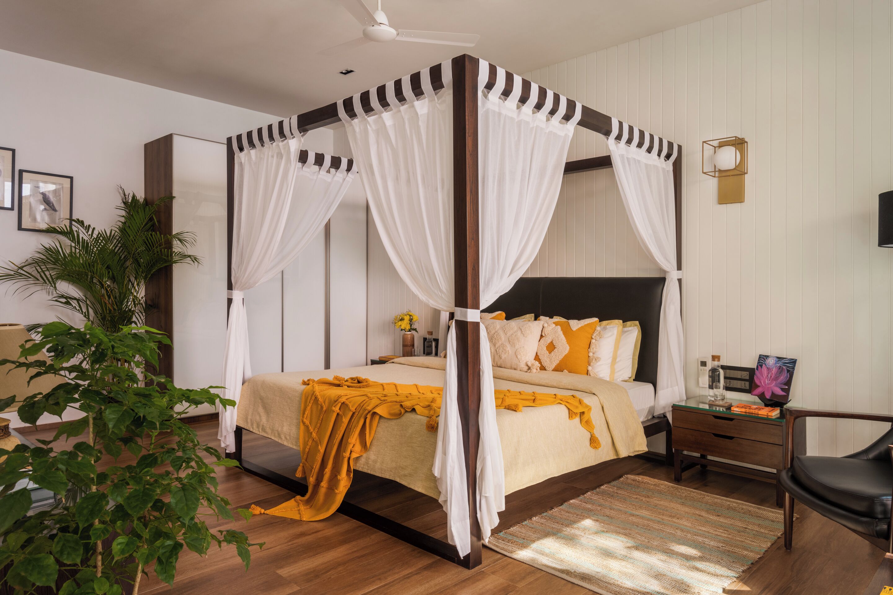 Ein Bett mit Baldachin und hölzernem Gestell, ein Nachttisch mit Lampe und ein Topfpflanze.