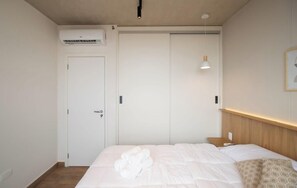 Ein Schlafzimmer mit einem Bett, einem Nachttisch, einer Wandleuchte, einer Klimaanlage und einer Tür.