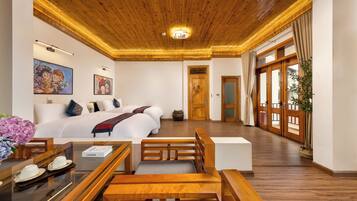 Quarto de hotel com teto de madeira, cama com roupa de cama branca, escrivaninha com cadeira e uma janela grande com cortinas.