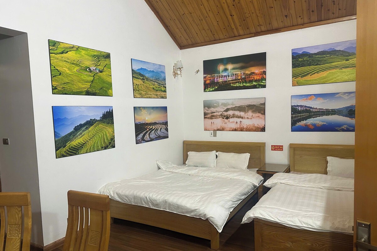 Quarto com cama e cadeira de madeira, e várias pinturas de paisagens nas paredes.