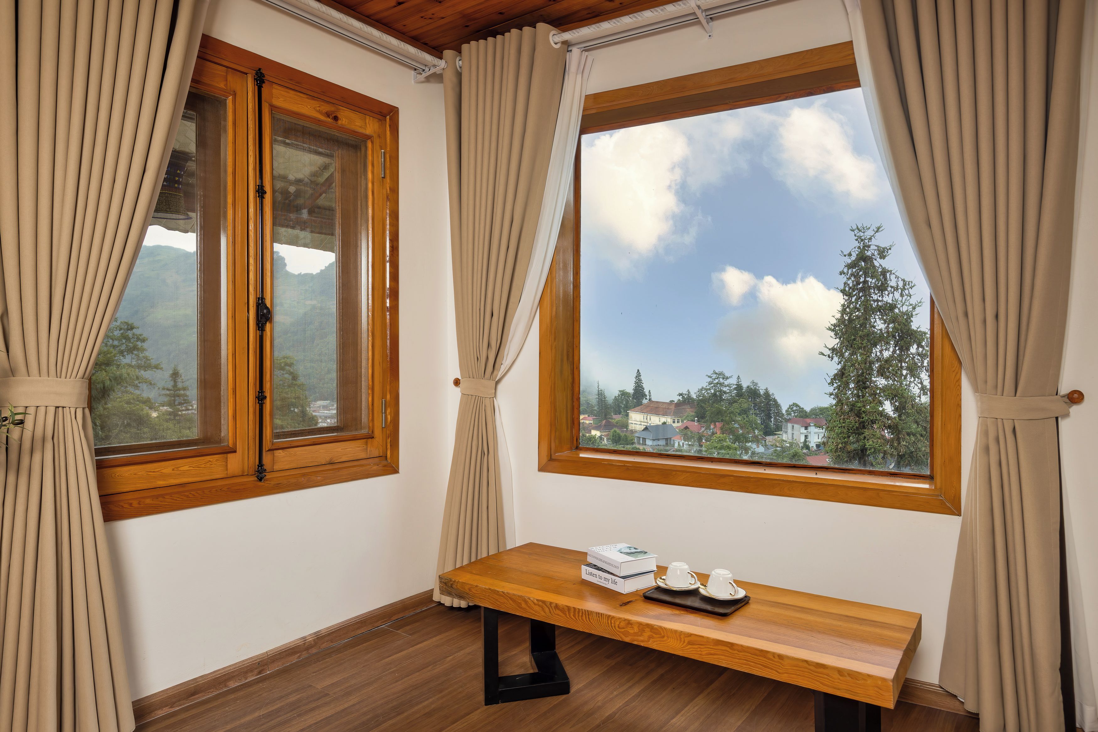 Una habitación con dos ventanas, una mesa de madera con una bandeja y tazas, y cortinas.