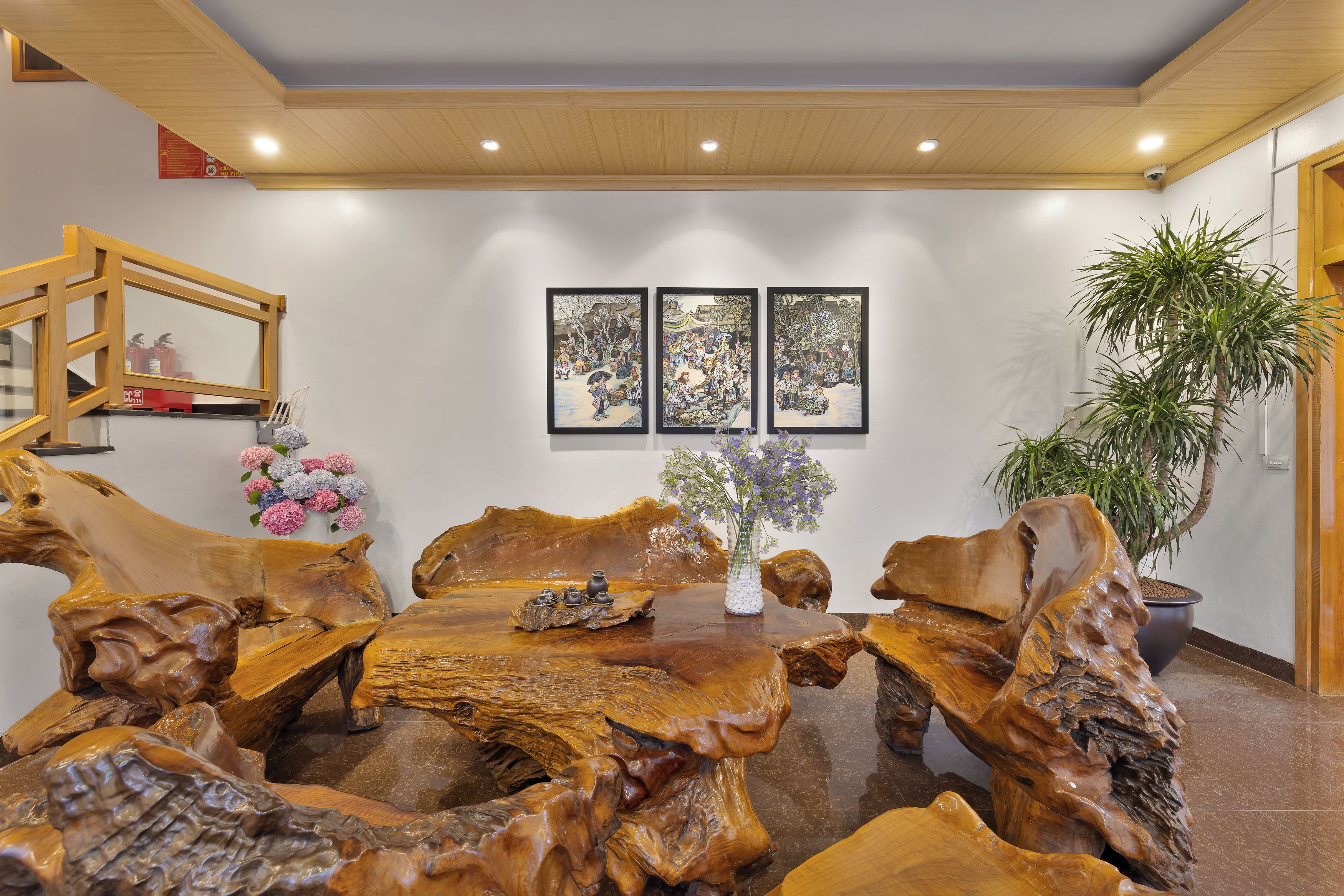 A dining area with a unique wooden table centerpiece, framed artwork on the wall, and a potted plant.
