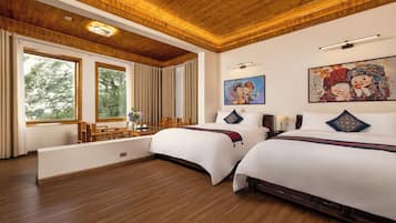 Ein Hotelzimmer mit zwei Betten, Holzboden, großen Fenstern mit Vorhängen und Bildern an den Wänden.