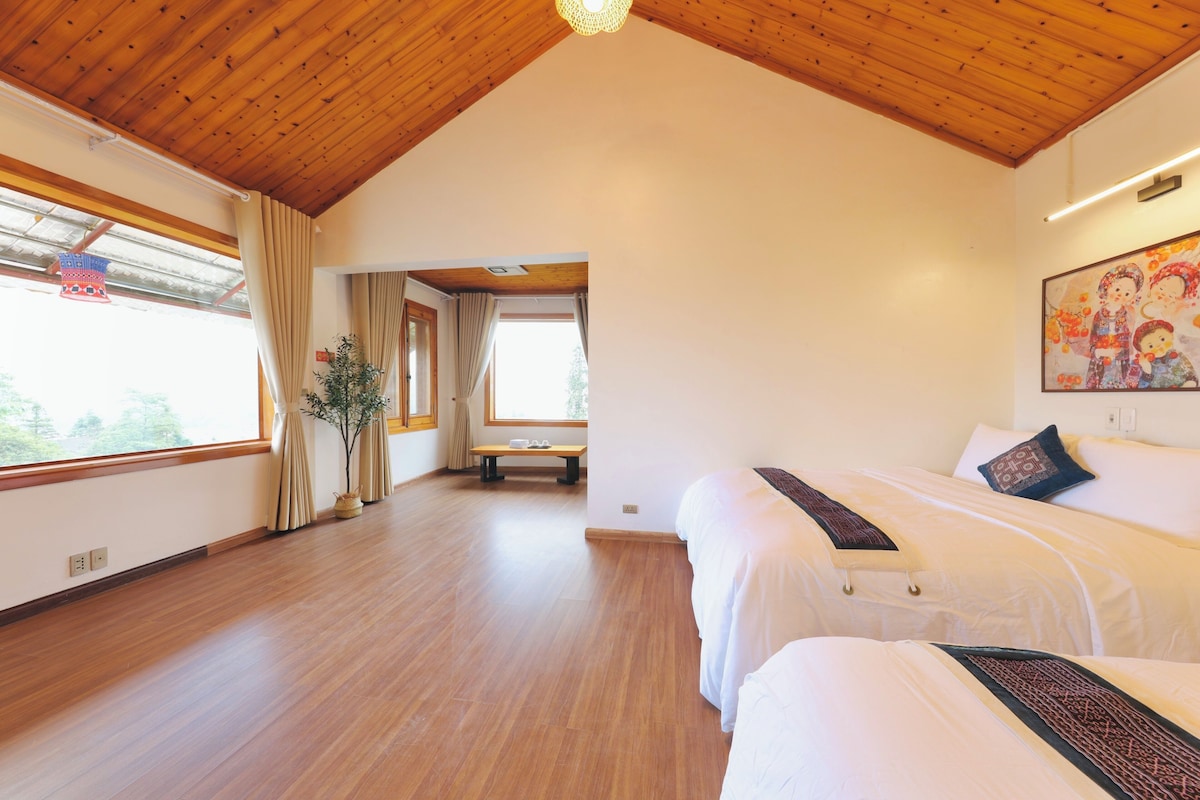 Habitación de hotel con suelo de madera, cama con ropa de cama blanca, un banco y un cuadro en la pared.