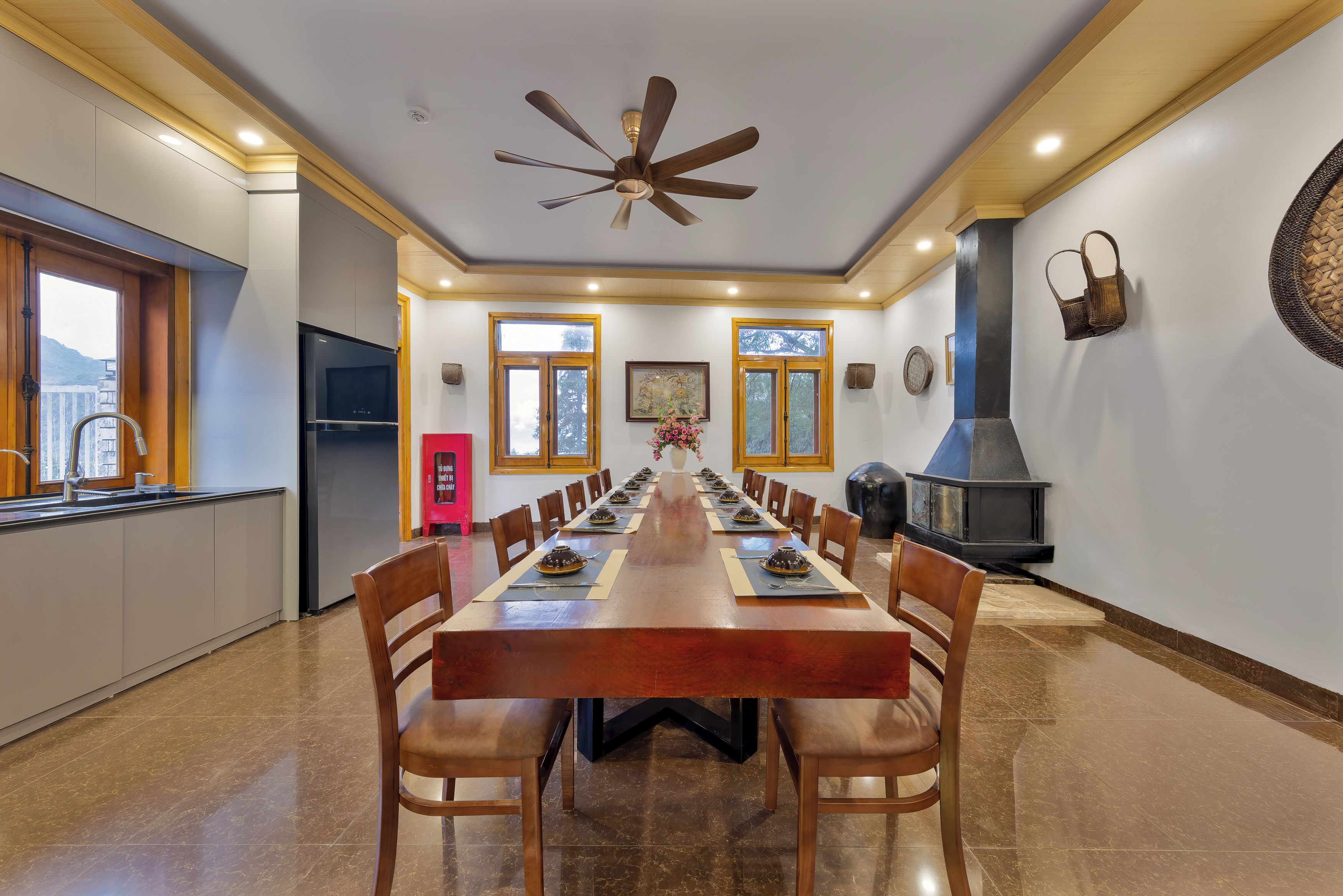 Un comedor con una larga mesa de madera, sillas, un ventilador de techo y una chimenea.