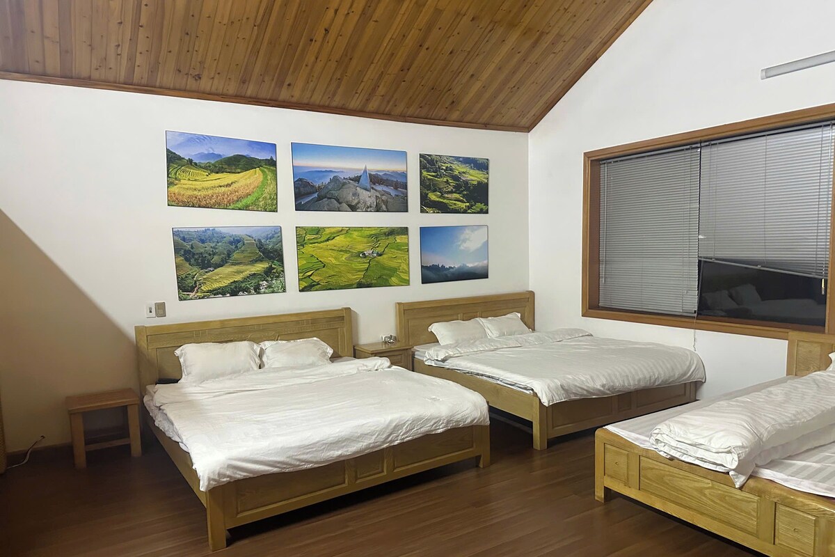 Quarto com três camas, cabeceiras de madeira e uma janela grande com persianas.