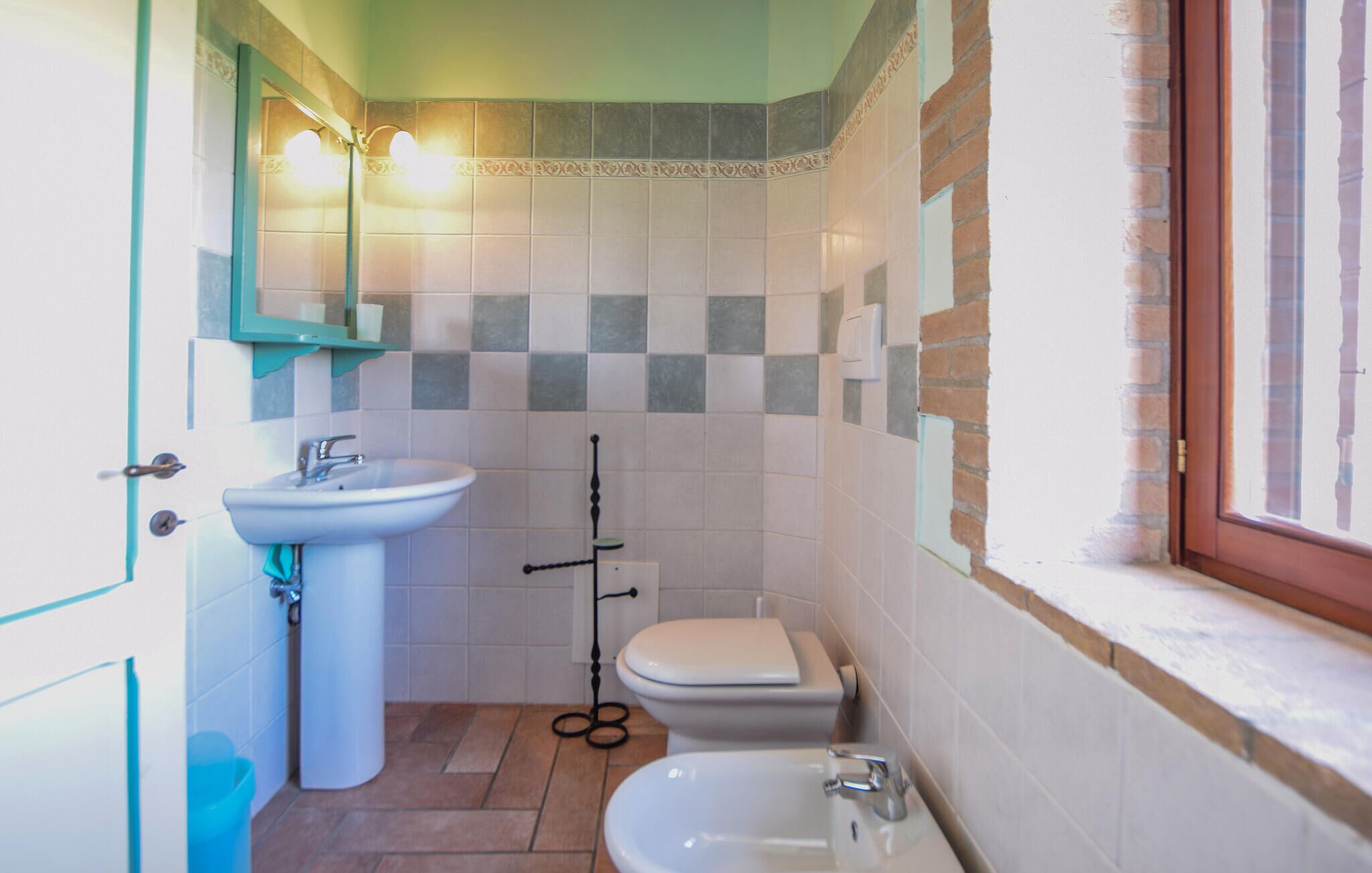 A compact bathroom with a sink, toilet, and bidet, featuring a tiled backsplash and a window.