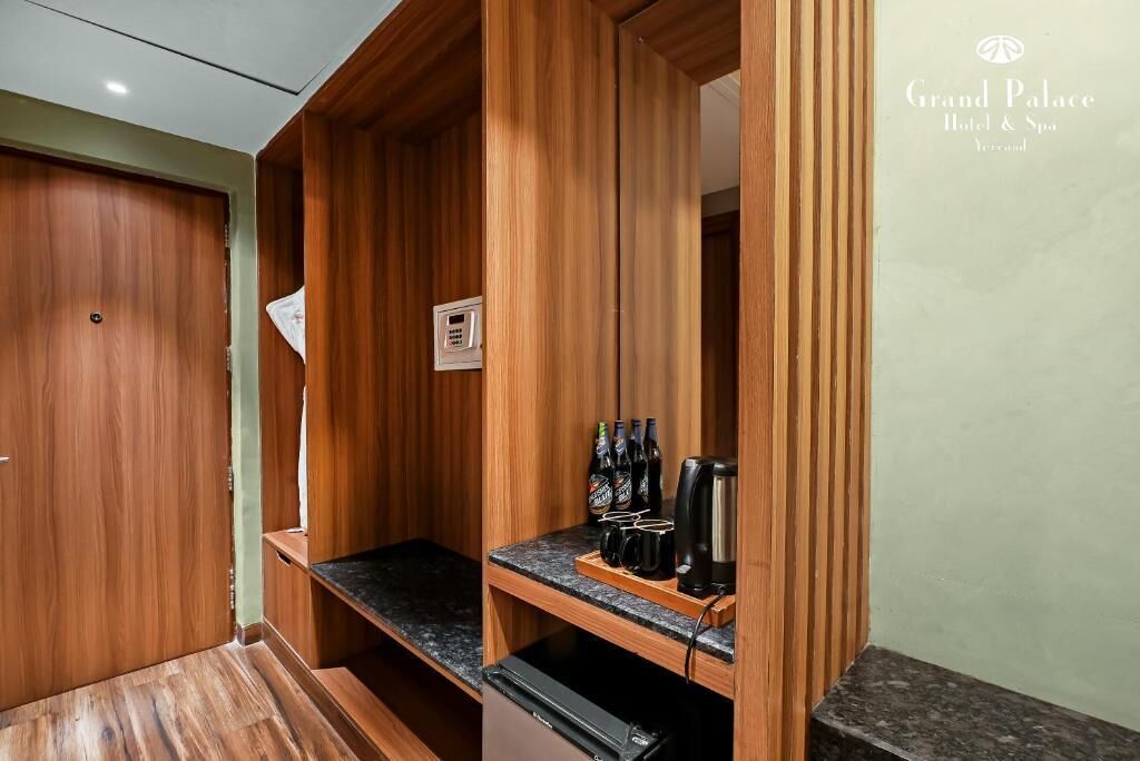 A wooden-paneled room with a built-in coffee station, a door with a keypad, and a small shelf with bottles and cups.