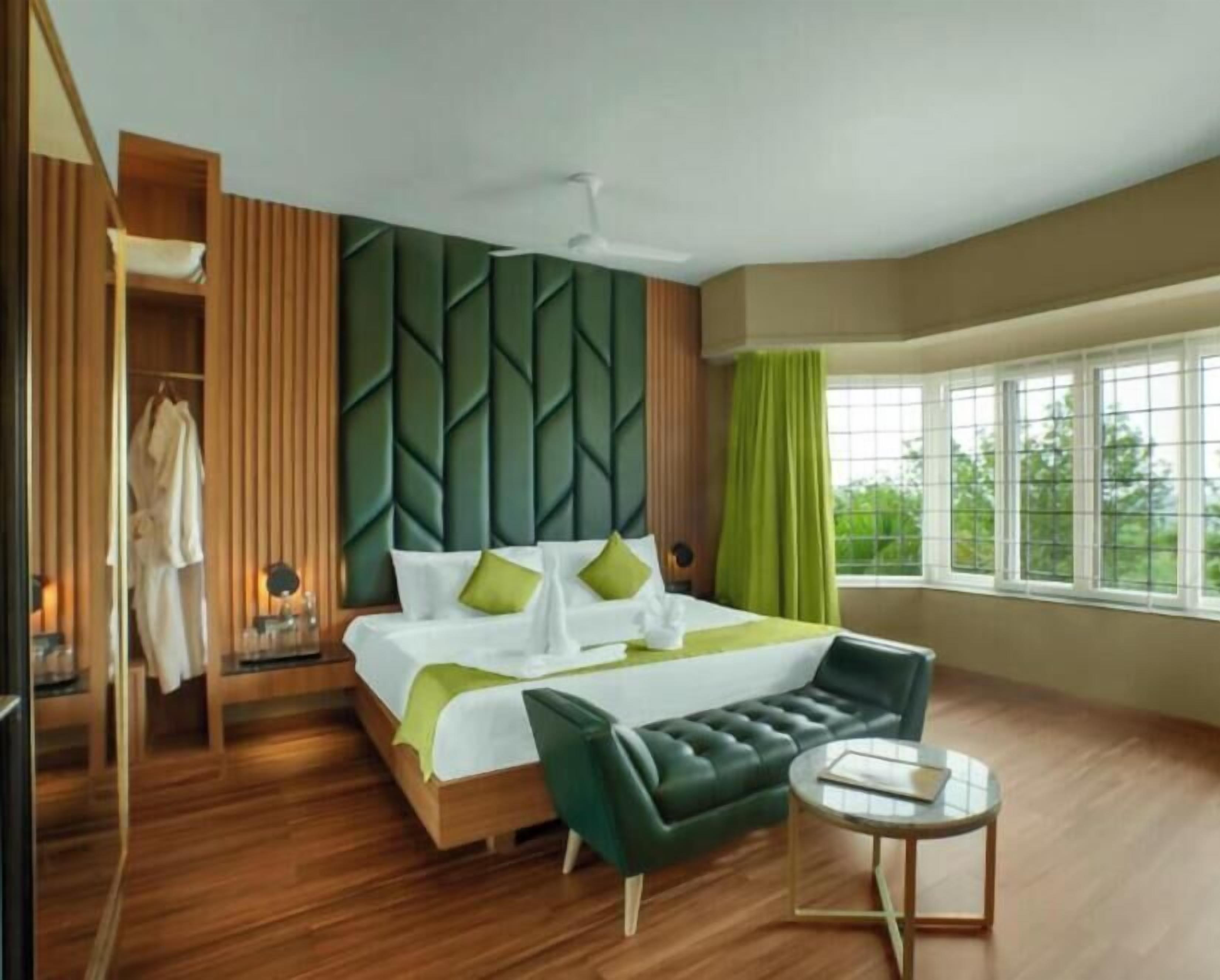 A hotel room with a bed, a green sofa, a small round table, and a window with a view.