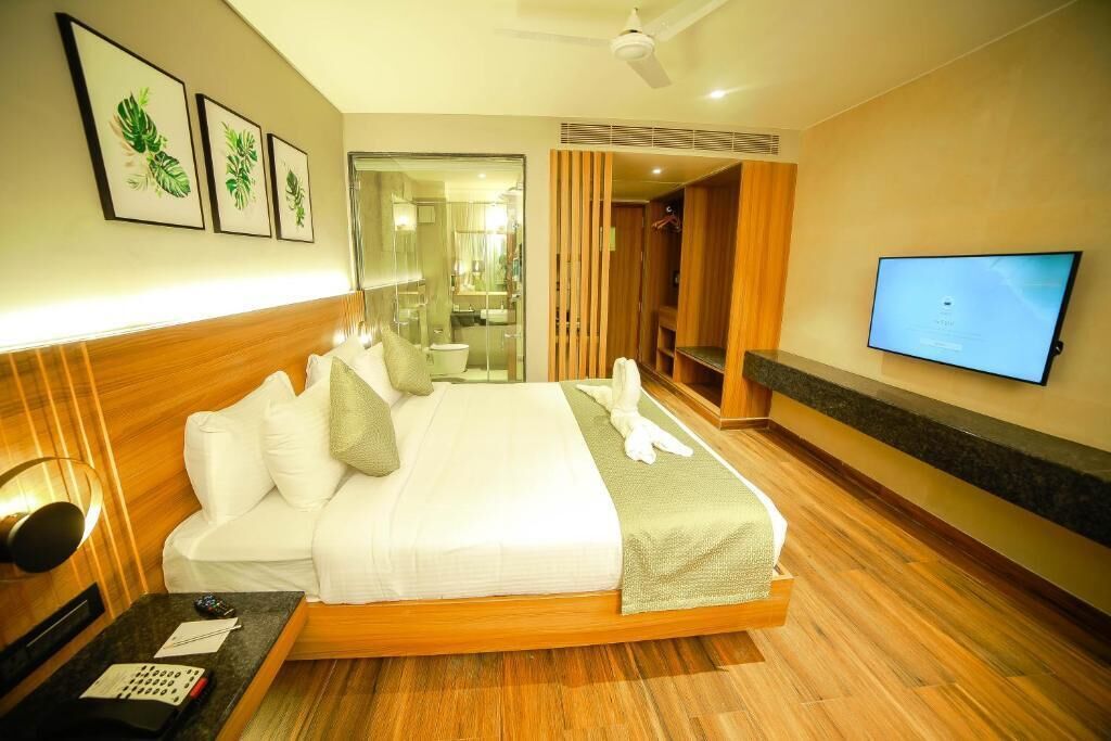 A hotel room with a bed, a TV, a desk with a phone, and a mirror.