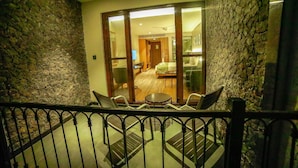 A balcony with a stone wall, a glass door leading to a room with a bed, a table, and chairs. - Grand Palace Yercaud (Yercaud)