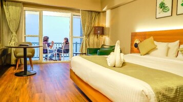 Habitación de hotel con una cama grande, una mesita, una silla, un balcón con vistas y piso de madera.
