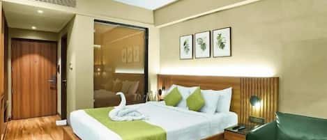 Una habitación de hotel con cama, un sillón verde, una mesita de noche con lámpara y un ventilador de techo.