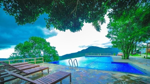 A swimming pool with lounge chairs, a stone deck, and a view of mountains. - Grand Palace Yercaud (Yercaud)