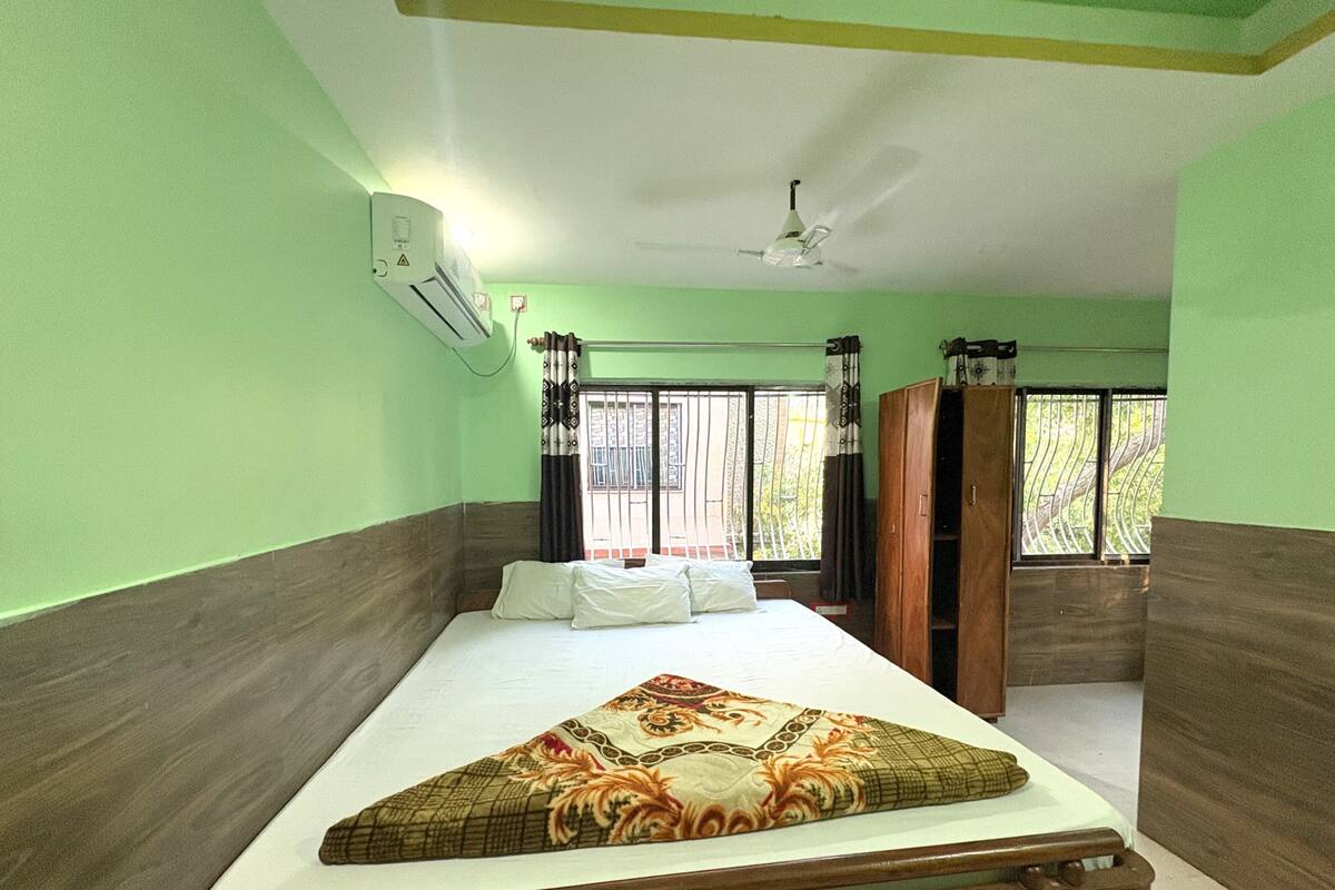 A room with a bed, an air conditioner, a window with metal bars, and a ceiling fan.