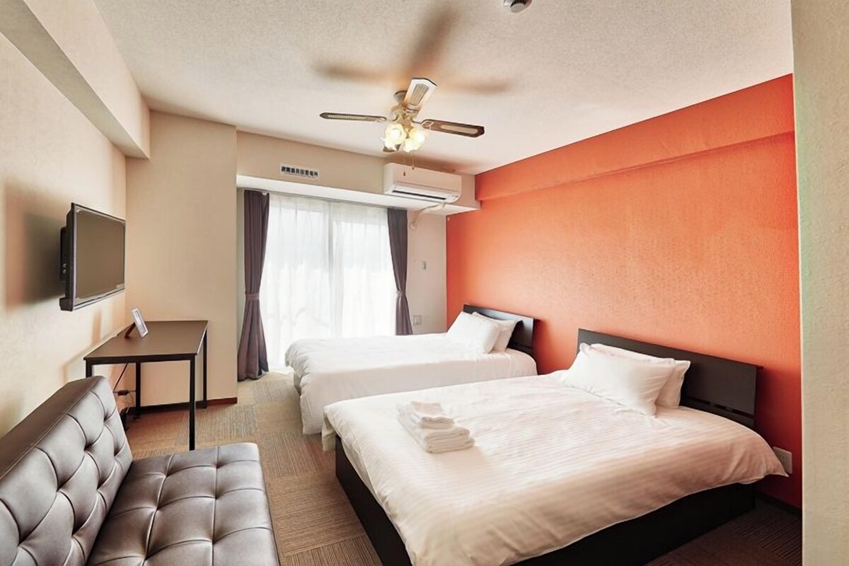 Une chambre d’hôtel avec deux lits, un canapé, une télévision et un ventilateur de plafond.