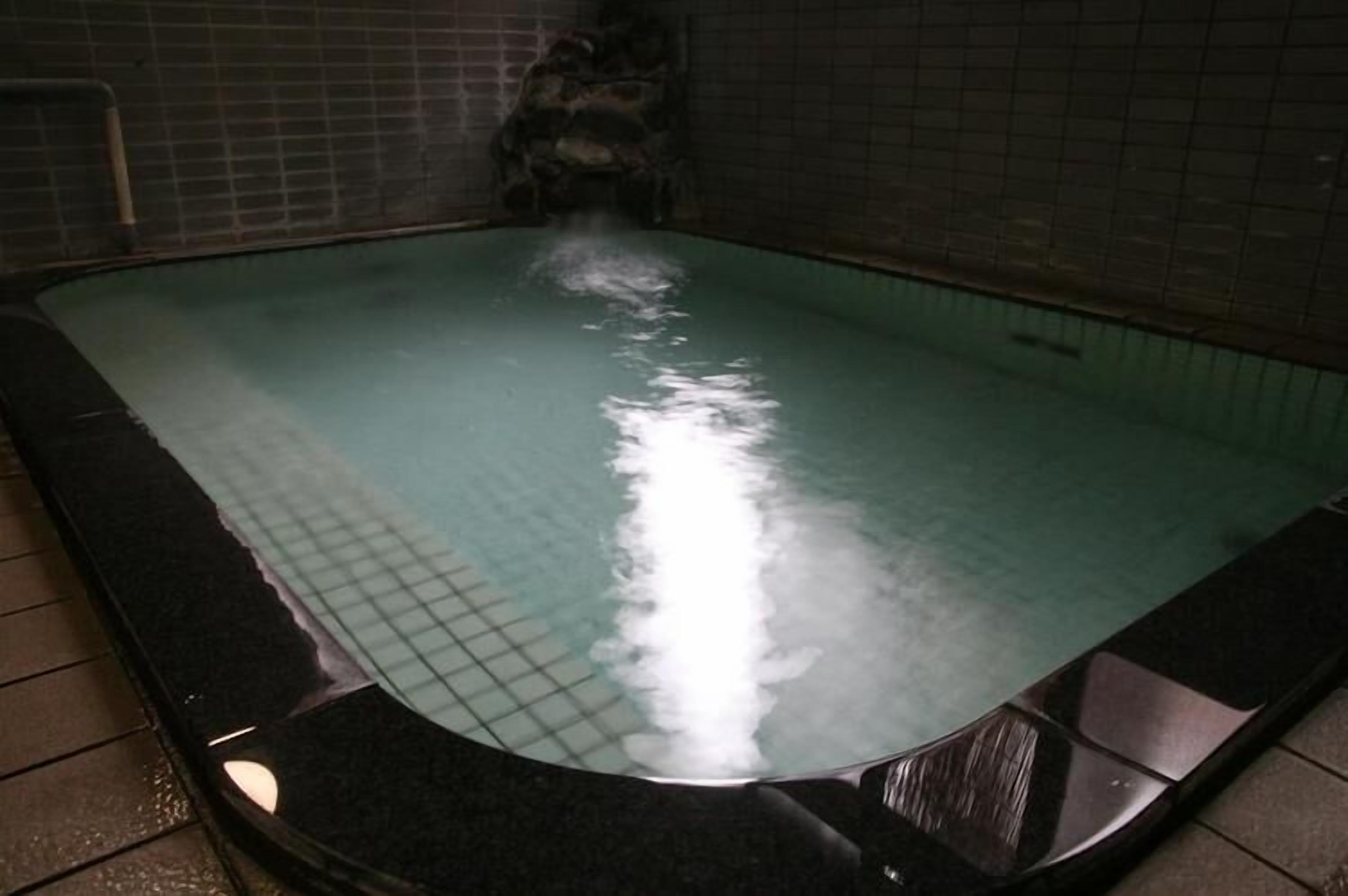 A hot tub with a tiled interior, a visible water jet, and a tiled wall.