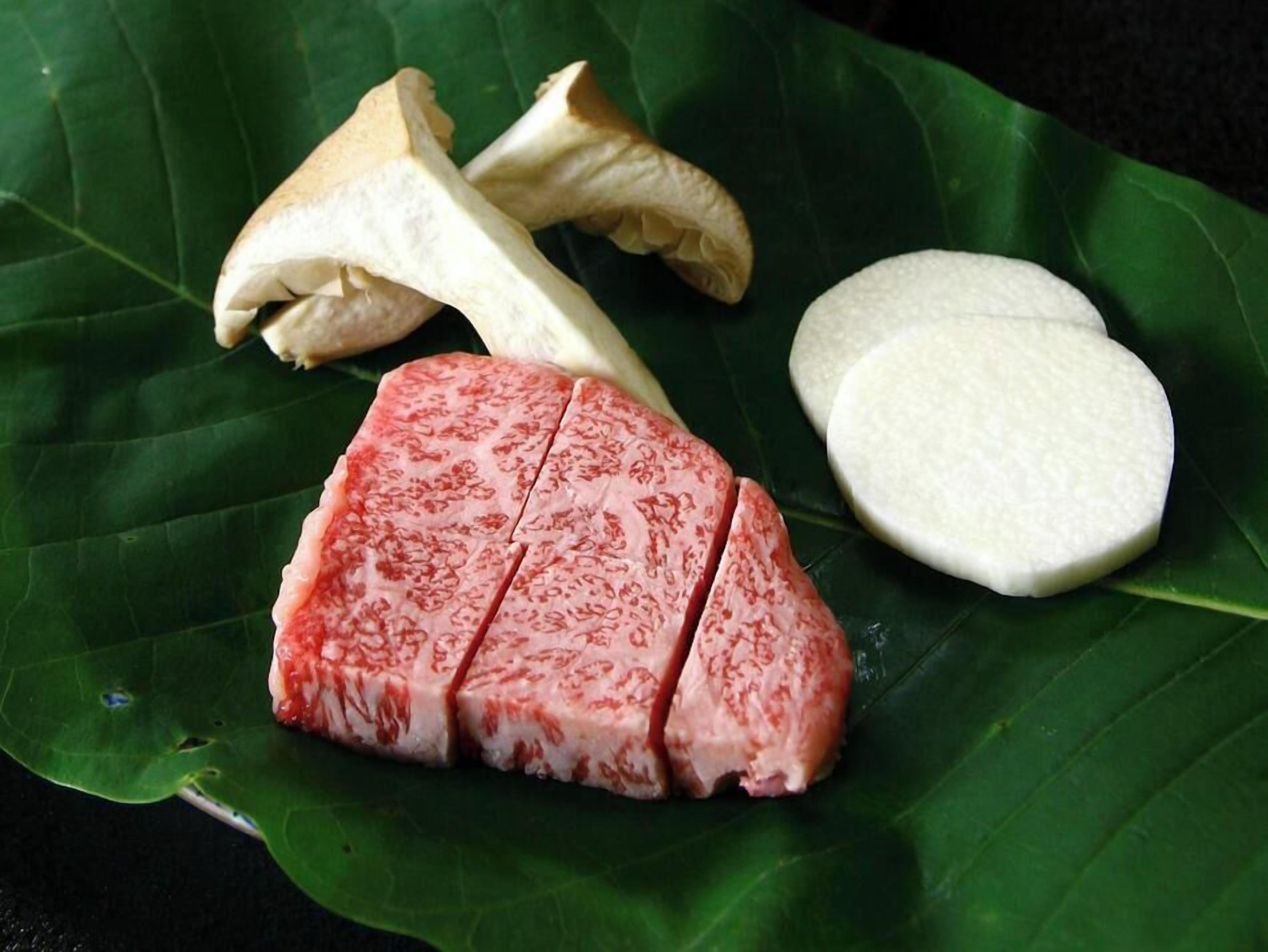 A piece of meat, a white round object, and a mushroom on a green leaf.