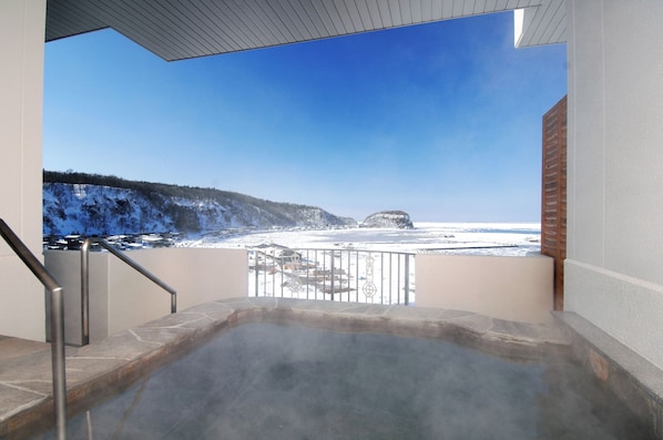 Uma banheira de hidromassagem com vista para uma paisagem nevada e um céu azul claro.