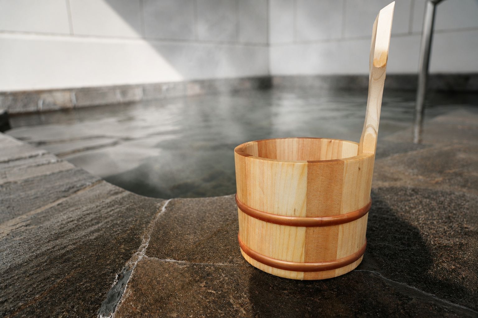 A wooden bucket with a handle on a stone floor near a body of water.