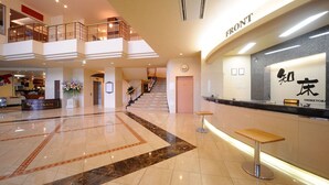 Vestíbulo de hotel con mostrador de recepción, una escalera y un cartel que indica la zona de entrada.