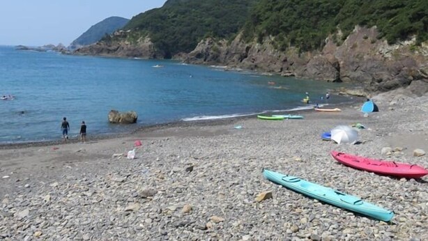 A rocky beach with kayaks and a tent.