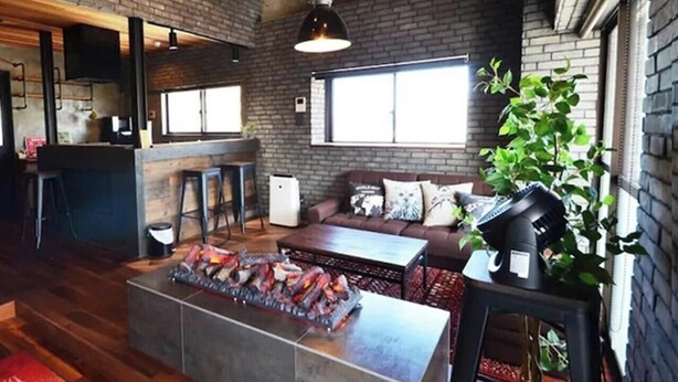 Een modern interieur met een bakstenen muur, een houten eethoek, een zithoek met open haard, en een groot raam dat natuurlijk licht binnenlaat.