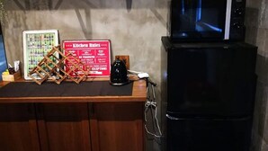 Een aanrecht met een bord waarop keukenregels staan, een koffiezetapparaat en een zwarte koelkast.
