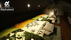 Een kamer met weinig licht, voorzien van drie bedden, elk met beddengoed en kussens met een patroon.