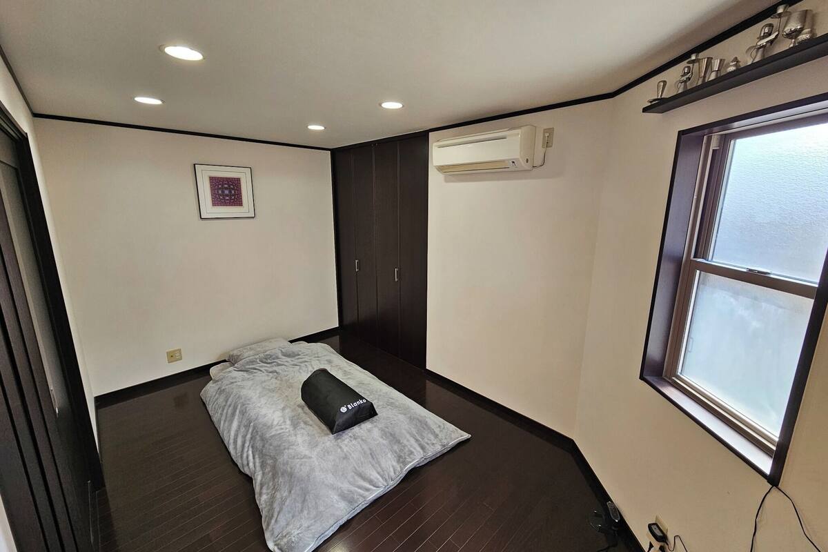 Una habitación pequeña y con poca luz, que tiene una cama, un ventanal y un equipo de aire acondicionado.