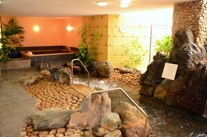 A hot spring area with a stone wall, rocks, and a wooden bench. - Haga Farm & Glamping (Haga)