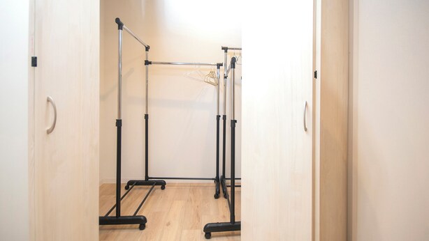 A room with a wooden floor, a metal rack with clothes, and a door with a handle. - K's Hotel (Takamatsu)