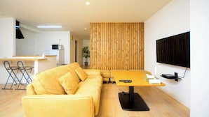 A modern living room with a sofa, a wooden partition, a TV, and a kitchen area in the background. - K's Hotel (Takamatsu)